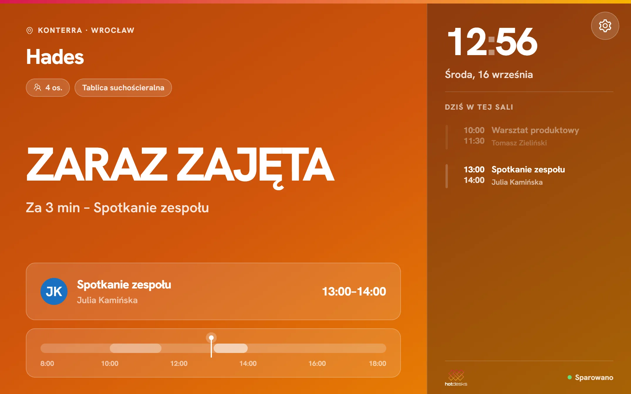 Monitor sali HotDesks na tablecie przy drzwiach: duży status zajętości, trwające spotkanie i agenda dnia
